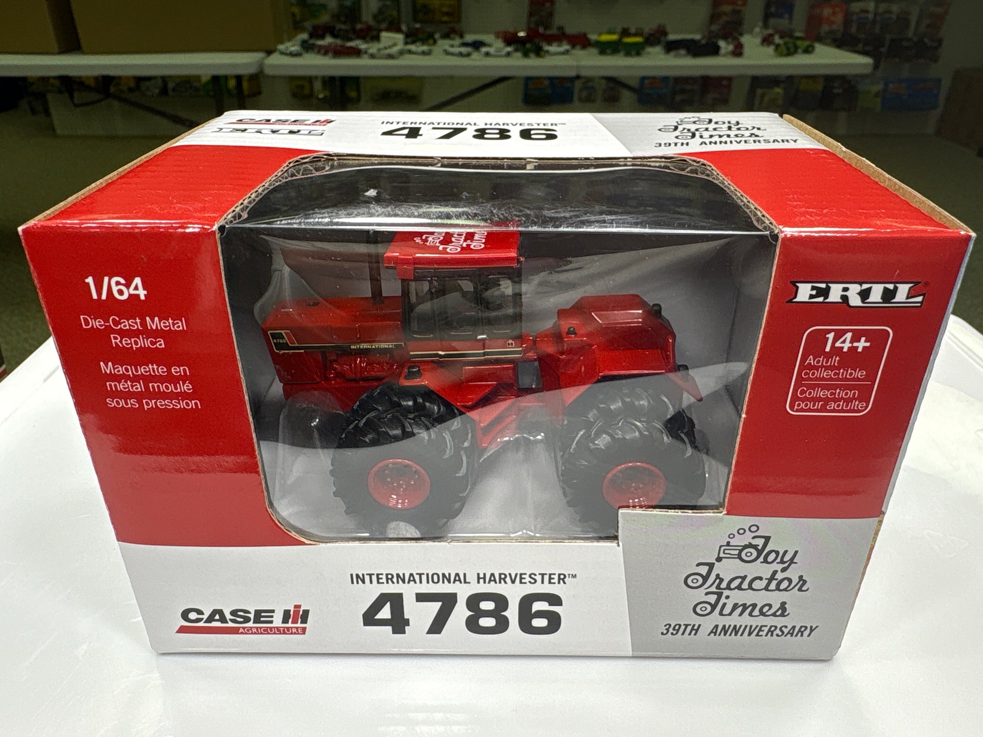 Red toy tractor in a box with ERTL branding on a white surface.